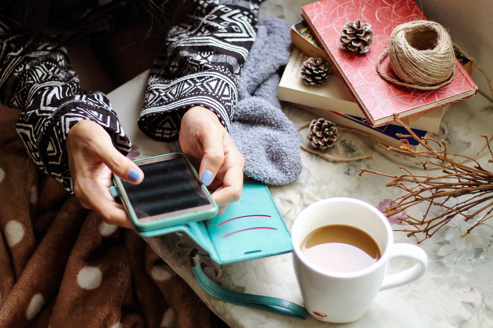 Frau mit Smartphone in der Hand, daneben ein Notizbuch und eine Tasse Kaffee